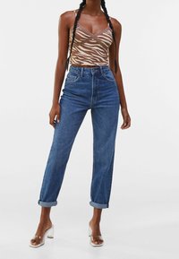 Top cropped a righe zebra marrone e beige con spalline regolabili, abbinato a jeans in denim blu a vita alta, con risvolti e tacchi trasparenti.