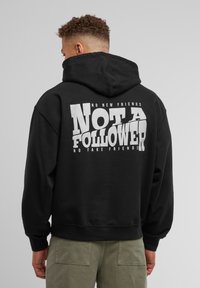 Hoodie noir avec un grand graphique blanc au dos comportant le texte "PAS UN SUIVEUR" et un texte plus petit au-dessus et en dessous.