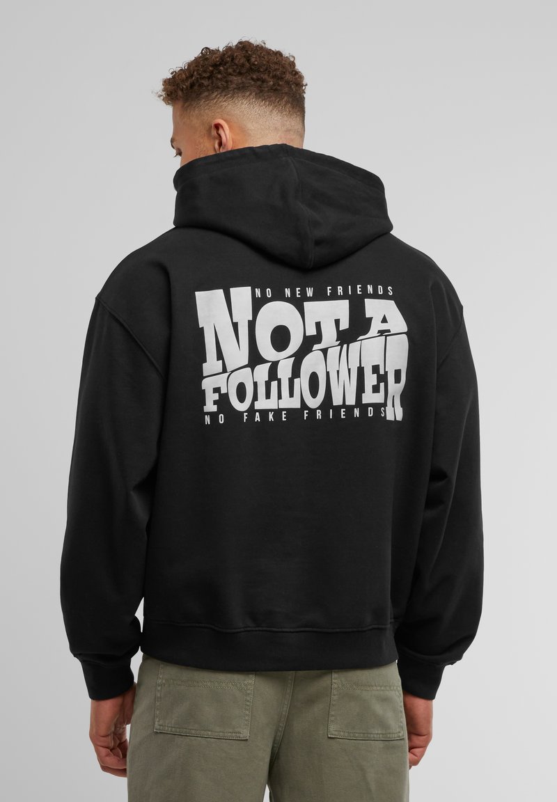 Hoodie noir avec un grand graphique blanc au dos comportant le texte "PAS UN SUIVEUR" et un texte plus petit au-dessus et en dessous.