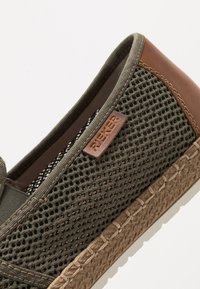 Olijfgroene mesh instapschoen met bruin leren accenten. Bevat een gestructureerde zool en gestikte details langs de rand.