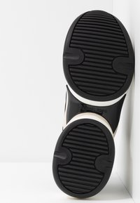 Semelle d'une basket noire et blanche avec des motifs texturés antidérapants, affichant le nom de la marque Michael Kors entre les zones du talon et des orteils.