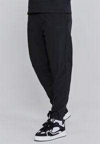 Schwarze Jogginghosen mit einer weichen, glatten Textur und elastischen Bündchen. Verfügt über ein dezentes Logo-Detail an der Seite und ein entspanntes Design.