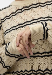 Maglione lavorato a maglia beige con motivo a righe nere. Presenta un design testurizzato simile a pizzo e polsini a coste. Vestibilità comoda con scollatura a girocollo.