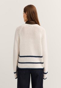 Strickpullover in Creme mit Marineblau gestreift, mit geripptem Saum und entspannter Passform. Strukturierter Stoff und Raglanärmel vervollständigen das legere Design.