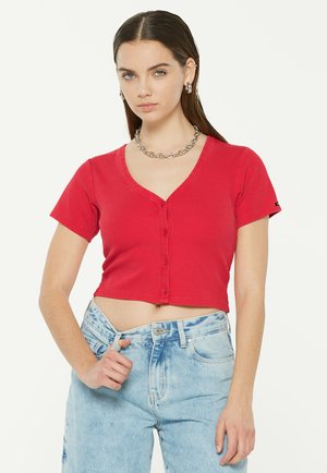 Rotes, kurzes Button-Up-Hemd mit kurzen Ärmeln, gerippter Textur und V-Ausschnitt. Kombiniert mit hellblauen, hoch taillierten Jeans.