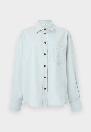 Camisa de ganga azul clara com mangas longas, fecho de botões, bolso no peito e um ajuste ligeiramente relaxado. Apresenta costuras em contraste e botões castanhos.