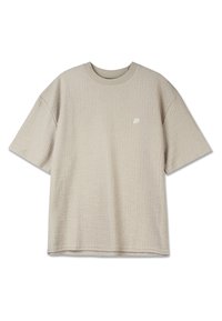 T-shirt beige clair à manches courtes en tissu texturé. Il présente un col rond et un petit logo blanc sur le côté gauche de la poitrine.