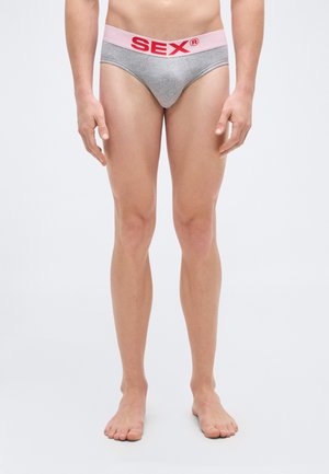 Grijze katoenen slips met een lichtroze tailleband waarop een opvallend rood "SEX" logo staat. De pasvorm is strak en ontworpen voor minimale bedekking.