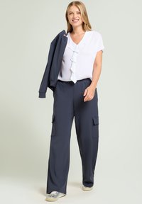 Ciemnoniebieskie spodnie o szerokich nogawkach z dwoma kieszeniami po bokach, w połączeniu z białą bluzką z falbanami. Na ramieniu noszona jest dopasowana ciemna marynarka.