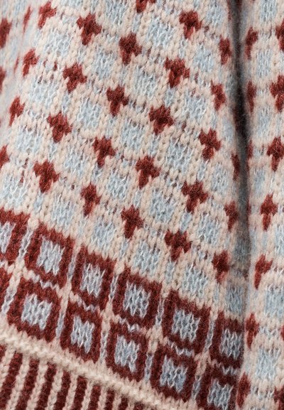 Κοντινό πλάνο πλεκτού υφάσματος με επαναλαμβανόμενο διακοσμητικό μοτίβο διαμαντιών σε κόκκινο, ανοιχτό μπλε και εκρού χρώματα σε πουλόβερ.