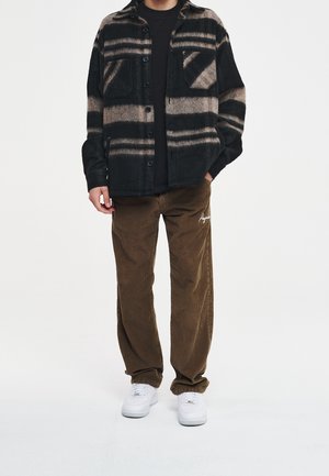 Zwart-bruine geruite flanellen blouse met twee borstzakken, gecombineerd met bruine ribfluwelen broek en witte sneakers, met een casual pasvorm.