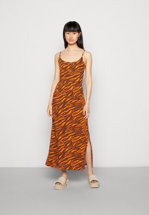 Vestido maxi em tecido castanho com riscas de tigre laranja, com alças finas e fenda lateral; combinado com sandálias de plataforma beje.