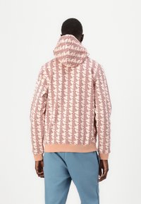Felpa con cappuccio in rosa morbido con un motivo geometrico rosso. Presenta un orlo e polsini a costine, progettata con una vestibilità comoda.