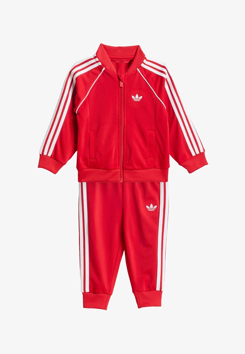 Piros tréningruha sima anyagból, fehér három csíkkal az ujjakon és a lábszárakon, kis fehér logóval a mellkason és a csípőn.