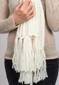 Sciarpa bianca lavorata a maglia con dettagli di frange, realizzata in filato morbido. La texture è spessa, con un motivo di trama aperta e sciolta.