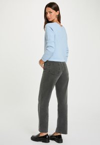 Hellblauer Strickpullover mit langen Ärmeln, kombiniert mit hochgeschnittenen grauen Jeans und schwarzen Slippers, von hinten betrachtet.