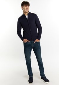 Jūras spēku zipsvārks ar ribotām piedurknēm un apakšmalu, apvienots ar zilām džinsām un jūras spēku sporta apaviem. Minimālists dizains, gluda tekstūra.