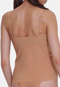 Nude-colored camisole with thin adjustable straps, soft fabric, and a fitted design. Smooth texture, minimal seams, and seamless back.