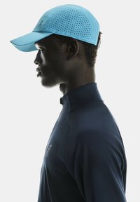 Lichtblauwe pet met perforaties op de kroon, gecombineerd met een donkerblauw shirt met hoge kraag. Schone lijnen en een gestroomlijnd ontwerp.