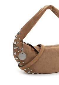 Bruin suède handtas met een gebogen handvat, zilveren studs langs de zijkant en een ritssluiting. Bevat een metalen label voor branding.
