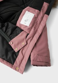 Light pink insulated jacket with black lining, quilted texture, snap buttons, and a label tag for size and care details.