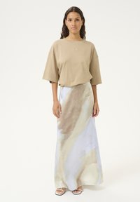 Beige oversized t-shirt in combinatie met een zwierige rok met een lichtblauw en bruin abstract patroon. De outfit accentueert een ontspannen pasvorm.