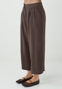 Bruine wijde broek met plooien, gemaakt van zachte stof. Gecombineerd met zwarte geweven ballerina's met een bandje en uitsnijdingen.