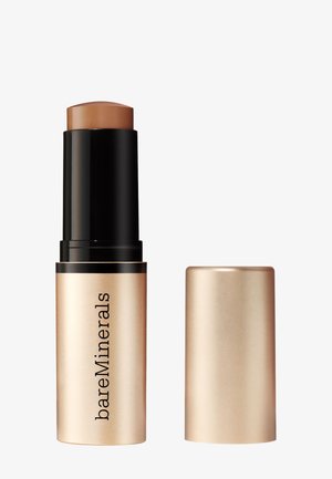 Bâton fond de teint mat avec le capuchon beige enlevé, révélant un produit crémeux marron moyen dans un tube noir et doré étiqueté bareMinerals.