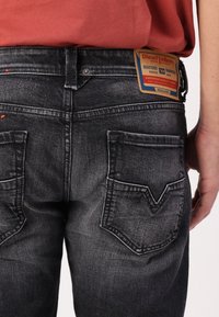 Svarta jeans i denim med en slitagen textur, utrustade med två bakfickor och en rektangulär etikett som visar texten "Diesel Industry."