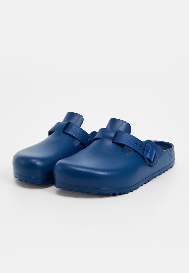 Ein Paar dunkelblaue Slipper-Clogs mit verstellbaren Riemen und strukturierten Sohlen, vor einem schlichten weißen Hintergrund.