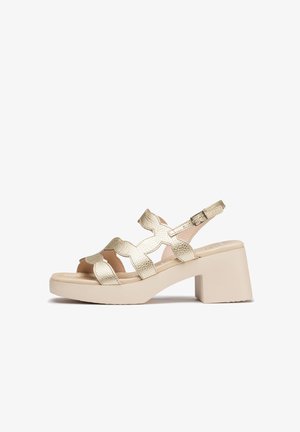 Sandalias texturizadas en dorado con tacón bloque y punta abierta que presentan correas entrecruzadas. Correa ajustable en el tobillo para un ajuste seguro. Suela beige clara.