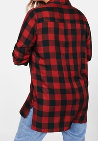 Koszula flanelowa w kratę w czerwono-czarnym kolorze, z klasycznym kołnierzykiem, długimi rękawami i dłuższym tyłem. Miękka tekstura z wzorem w kratkę.