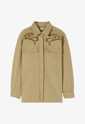 Camicia marrone chiaro a maniche lunghe con due tasche sul davanti e ricamo decorativo vicino alle spalle, con polsini e colletto con bottoni.