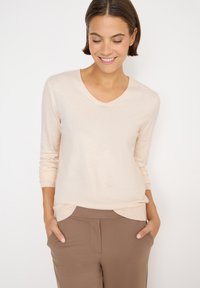 Hellbeige langärmliger V-Ausschnitt-Pullover aus weichem Material, mit gerippten Bündchen und lockerer Passform, kombiniert mit braunen Hosen.