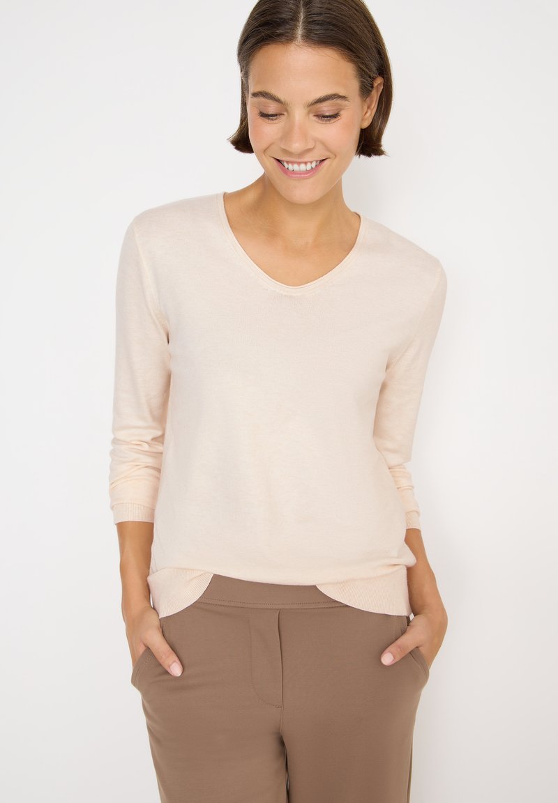 Hellbeige langärmliger V-Ausschnitt-Pullover aus weichem Material, mit gerippten Bündchen und lockerer Passform, kombiniert mit braunen Hosen.