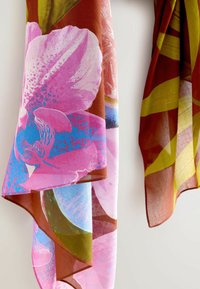 Kwiecisty szalik w różowych, niebieskich i ziemistych odcieniach o przezroczystej fakturze. Zawiera duże abstrakcyjne wzory kwiatowe oraz wyraziste paski w ciepłych kolorach.