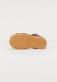 Brune lærersko med et intrikat utskjæringsdesign. Gummisålen har et lekent mønster med runde former og teksturer.