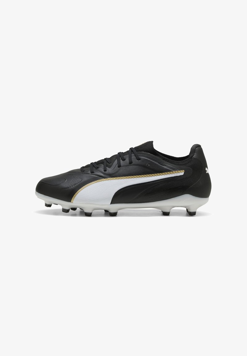 Chaussure de football noir et blanc avec garniture dorée, crampons moulés, col bas et lacets, conçue pour jouer sur terrain ferme.