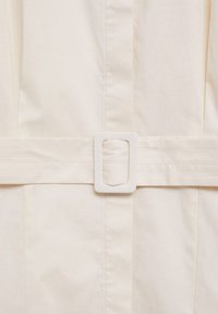 Ceinture en tissu crème avec une boucle rectangulaire blanche, présentant des lignes épurées et des détails de couture subtils. Texture lisse sans motifs.