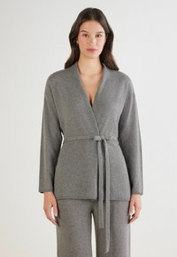 Cárdigan envolvente gris de punto, hecho de material suave, con un cinturón en la cintura, mangas largas y un diseño de escote en V.