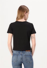 Tricou negru scurt, cu decolteu rotund și mâneci scurte, asociat cu blugi albaștri ajustați, care au buzunare la spate și o etichetă din piele.