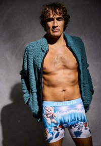 Boxers à imprimé ours en peluche bleus avec une taille bleu clair étiquetée "PULLIN", portés sous une veste zippée verte et duveteuse.