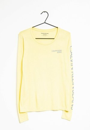 Langærmet gul bomuldsbluse med rund halsudskæring. Har lys blå "Calvin Klein Jeans" tekst på brystet og ærmet.