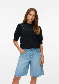 Svart blus med puffärmar, spetsdetaljer och strukturtyg, kombinerad med ljusblå denim bermudashorts med skräddarsydd passform.