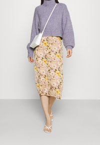 Lila stickad kortärmad tröja med långa ärmar, ihop med en rosa blommig midikjol som har gula och vita blommor. Vita sandaler och väska.