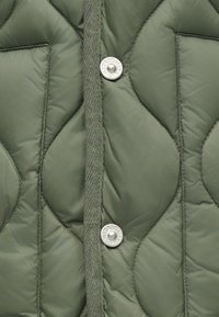 Geacă puf cu umplutură, de culoare verde măslin, cu un material matlasat și un model texturat, având două butoane de prindere argintii și o clapetă frontală țesută.