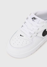 Sapatilha branca de couro com o logo da Nike em preto, biqueira perfurada, atacadores brancos planos, sola de borracha e marcação na lingueta.
