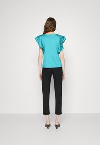 Top turquesa con mangas con volantes, combinado con pantalones negros. El top presenta un diseño de cuello redondo, mientras que los zapatos tienen punta afilada.