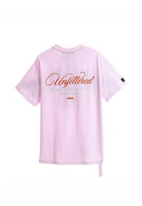 Camiseta corta de manga con cuello redondo en color rosa, que presenta un texto bordado en la parte posterior: “Sin ataduras” en color naranja y texto adicional debajo.