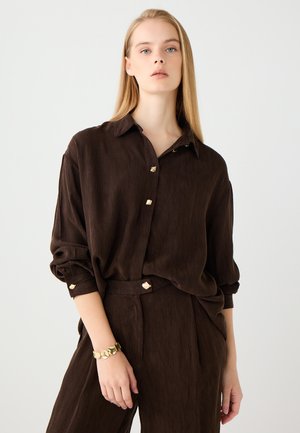 Brown button-up shirt made from textured fabric, featuring gold-tone buttons and rolled sleeves, paired with matching brown pants.